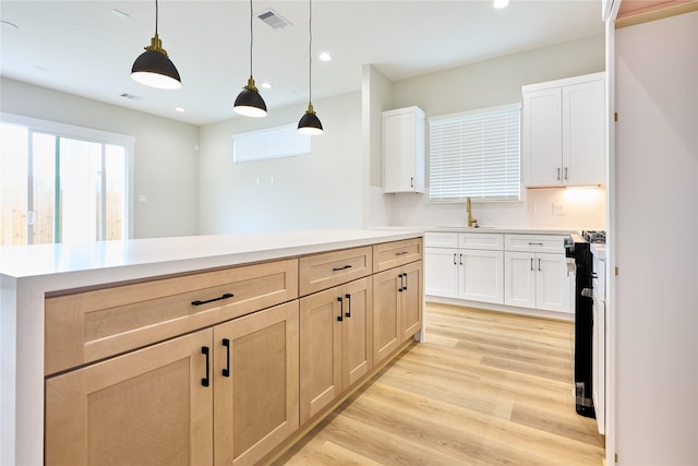 kitchen with sink, hanging light fixtures, light brown cabinets, light hardwood / wood-style floors, and stove