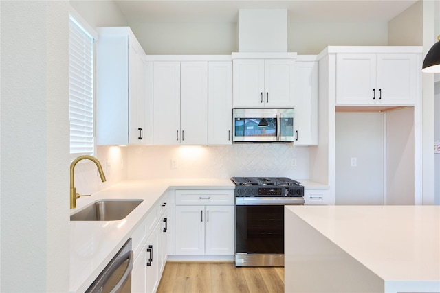 kitchen featuring appliances with stainless steel finishes, white cabinetry, sink, backsplash, and light hardwood / wood-style floors