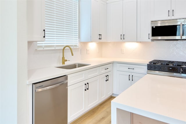 kitchen featuring appliances with stainless steel finishes, tasteful backsplash, white cabinetry, sink, and light wood-type flooring