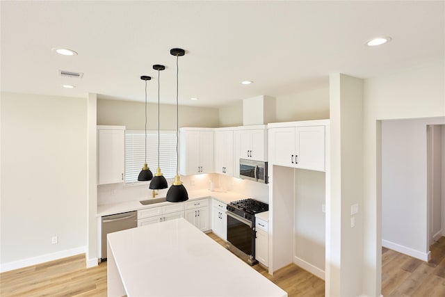 kitchen with white cabinetry, a center island, light hardwood / wood-style flooring, appliances with stainless steel finishes, and pendant lighting