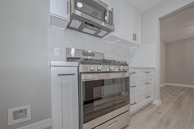 kitchen with white cabinets, light wood-type flooring, backsplash, and stainless steel appliances