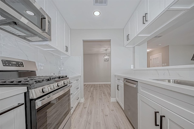 kitchen featuring sink, appliances with stainless steel finishes, decorative backsplash, white cabinets, and light wood-type flooring