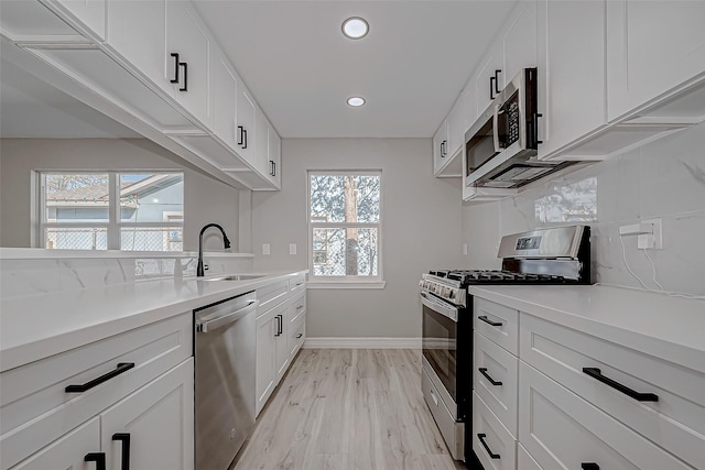 kitchen with light wood-type flooring, tasteful backsplash, stainless steel appliances, sink, and white cabinets