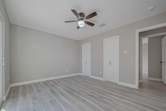 unfurnished bedroom featuring ceiling fan, light wood-type flooring, and two closets