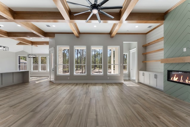 unfurnished living room with ceiling fan with notable chandelier, lofted ceiling with beams, wooden walls, light hardwood / wood-style flooring, and a fireplace