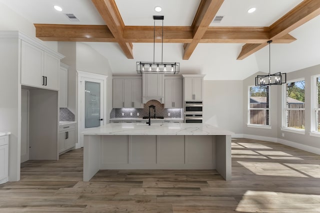 kitchen featuring a large island with sink, tasteful backsplash, light stone counters, and light hardwood / wood-style floors