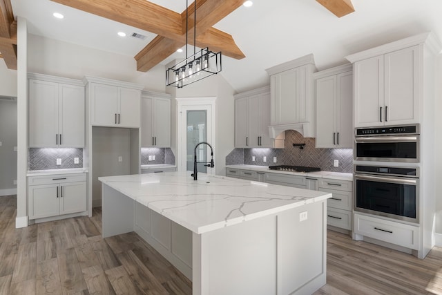 kitchen with beam ceiling, a kitchen island with sink, white cabinets, and light stone counters