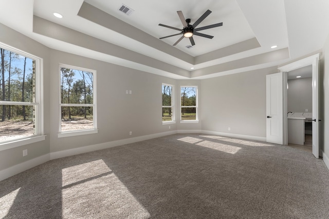 unfurnished bedroom with ceiling fan, carpet floors, multiple windows, and a tray ceiling