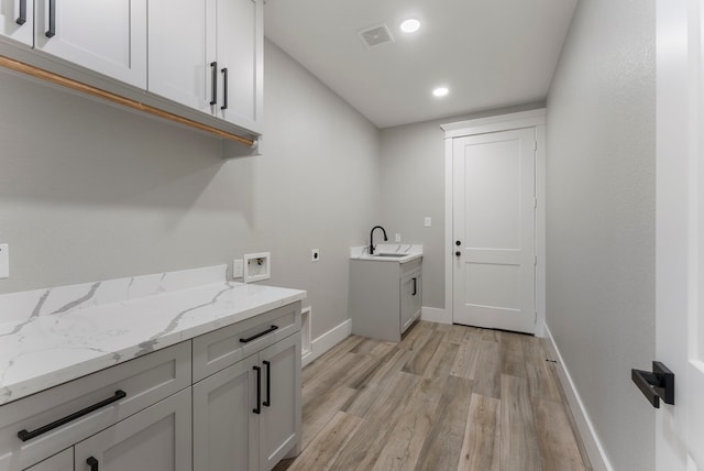 clothes washing area featuring cabinets, sink, hookup for a washing machine, light wood-type flooring, and hookup for an electric dryer