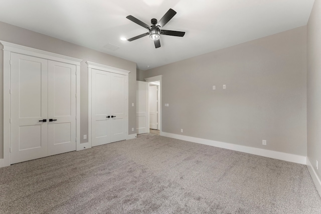 unfurnished bedroom with carpet, ceiling fan, and multiple closets