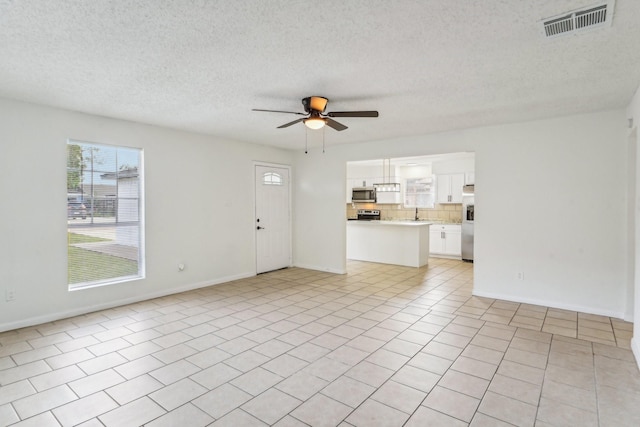 unfurnished living room featuring ceiling fan, light tile patterned floors, and a textured ceiling