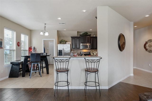 kitchen with dark brown cabinetry, hanging light fixtures, a chandelier, a kitchen bar, and appliances with stainless steel finishes