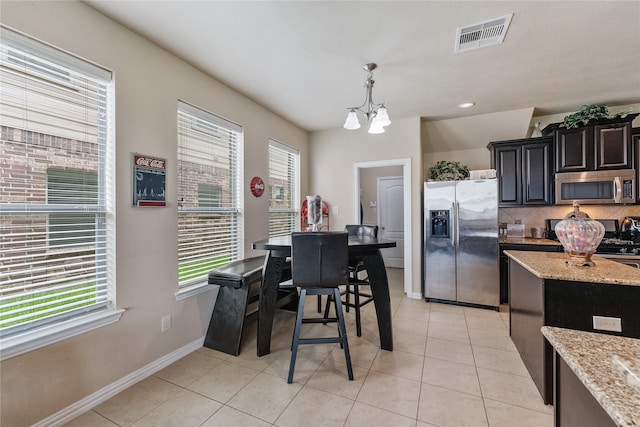 kitchen with light stone countertops, a notable chandelier, decorative light fixtures, a kitchen island, and appliances with stainless steel finishes