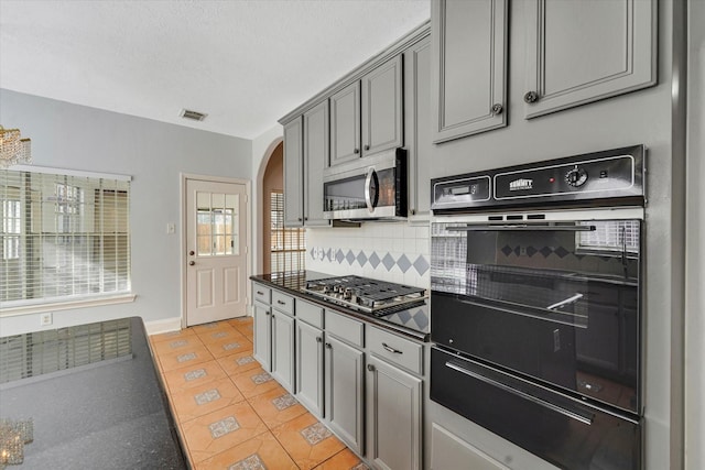 kitchen featuring backsplash, a textured ceiling, gray cabinets, light tile patterned flooring, and appliances with stainless steel finishes