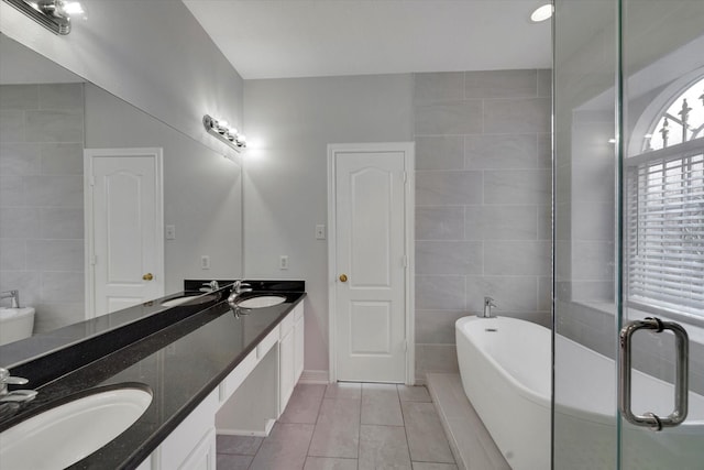 bathroom featuring vanity, a tub to relax in, tile patterned floors, and tile walls