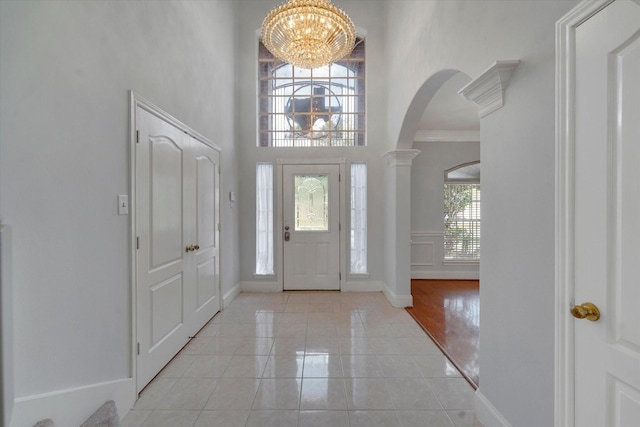 tiled foyer entrance featuring a notable chandelier, ornamental molding, and ornate columns