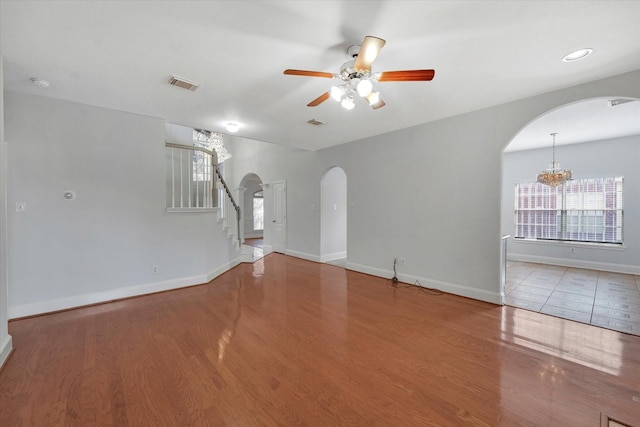 unfurnished living room with ceiling fan with notable chandelier and light hardwood / wood-style flooring