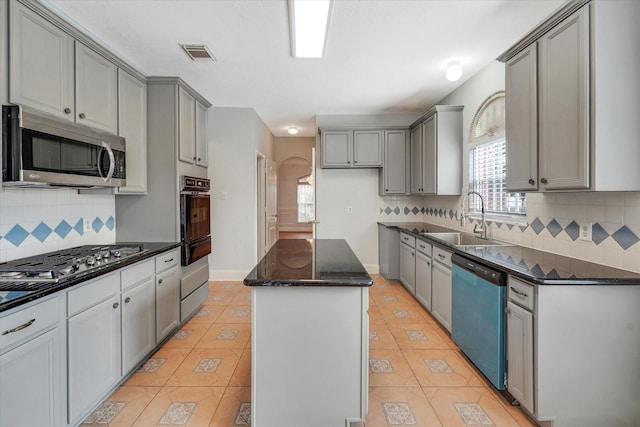 kitchen with gray cabinetry, a center island, sink, decorative backsplash, and appliances with stainless steel finishes