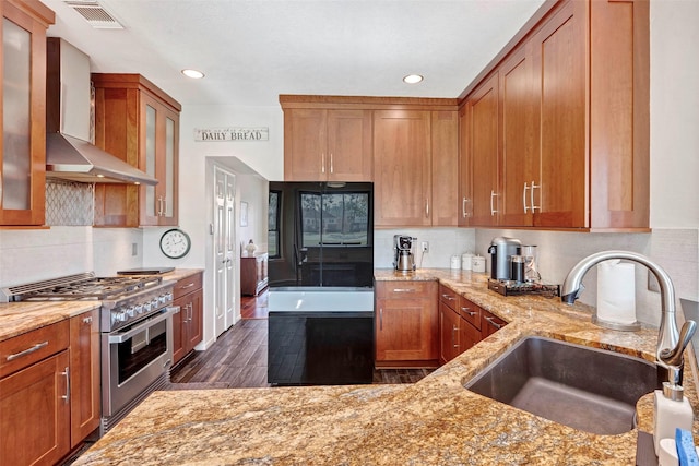 kitchen with range with two ovens, wall chimney range hood, sink, decorative backsplash, and light stone countertops