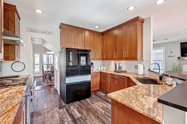 kitchen featuring kitchen peninsula, light stone countertops, black refrigerator, extractor fan, and sink