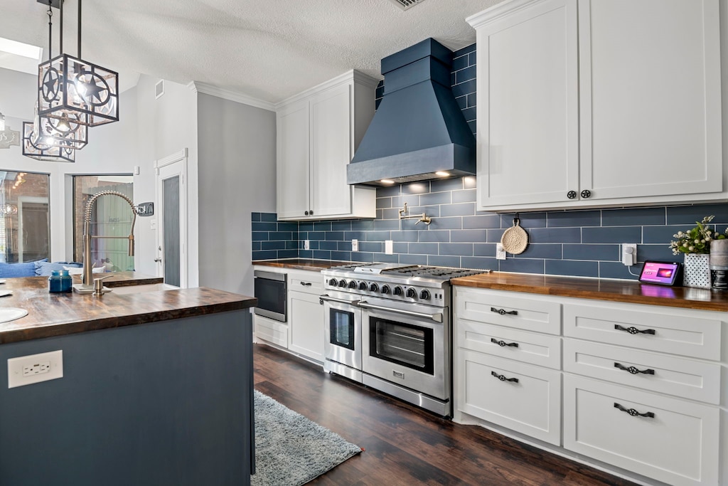 kitchen featuring premium range hood, butcher block counters, white cabinets, range with two ovens, and hanging light fixtures