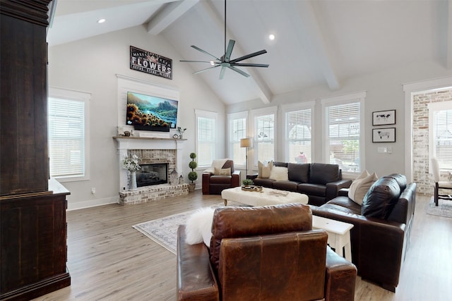 living room with ceiling fan, high vaulted ceiling, light hardwood / wood-style flooring, beamed ceiling, and a fireplace