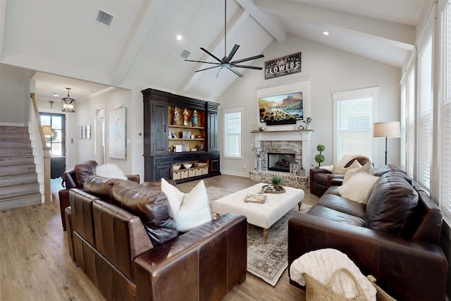 living room with a brick fireplace, ceiling fan with notable chandelier, high vaulted ceiling, light hardwood / wood-style flooring, and beamed ceiling