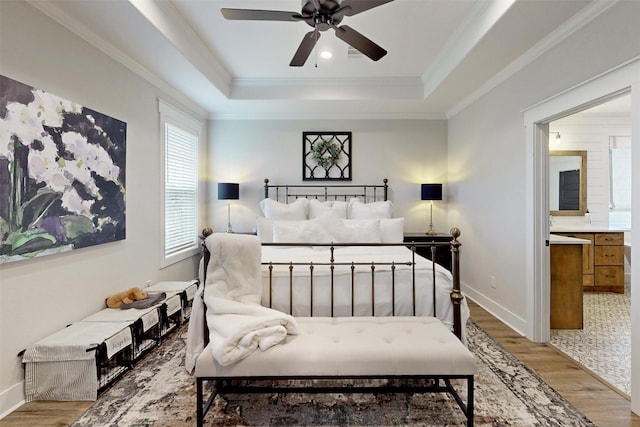 bedroom with wood-type flooring, connected bathroom, a raised ceiling, and ceiling fan