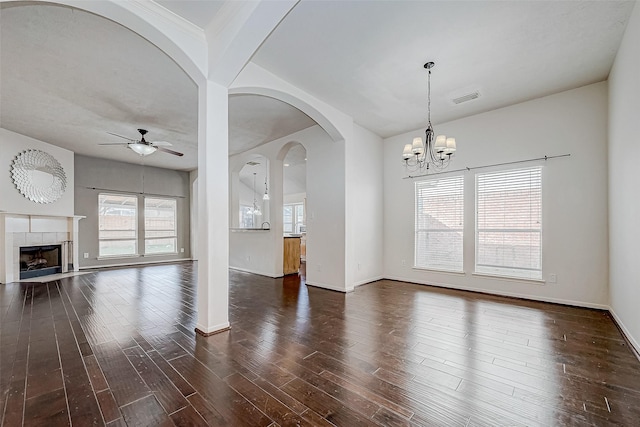 unfurnished living room featuring a tile fireplace, ceiling fan with notable chandelier, dark hardwood / wood-style floors, and a wealth of natural light