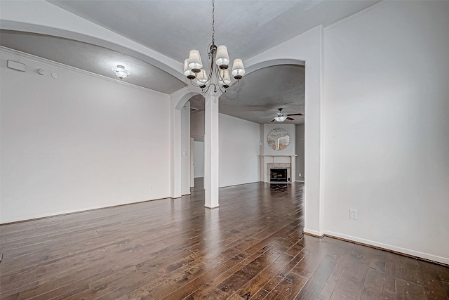 unfurnished dining area featuring a tile fireplace, ceiling fan with notable chandelier, and dark wood-type flooring