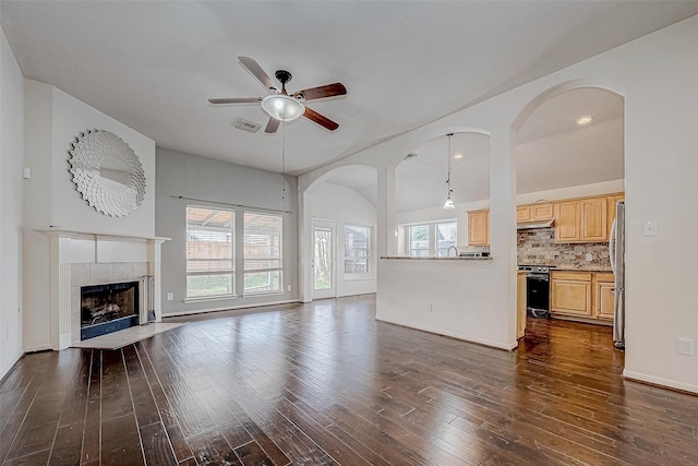 unfurnished living room with ceiling fan, dark hardwood / wood-style floors, vaulted ceiling, and a tiled fireplace