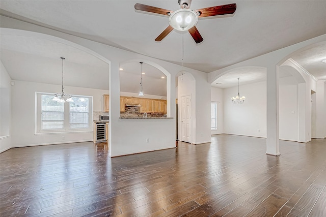 unfurnished living room featuring dark wood-type flooring, beverage cooler, and ceiling fan with notable chandelier