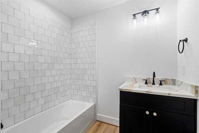 bathroom with wood-type flooring, vanity, and tiled shower / bath