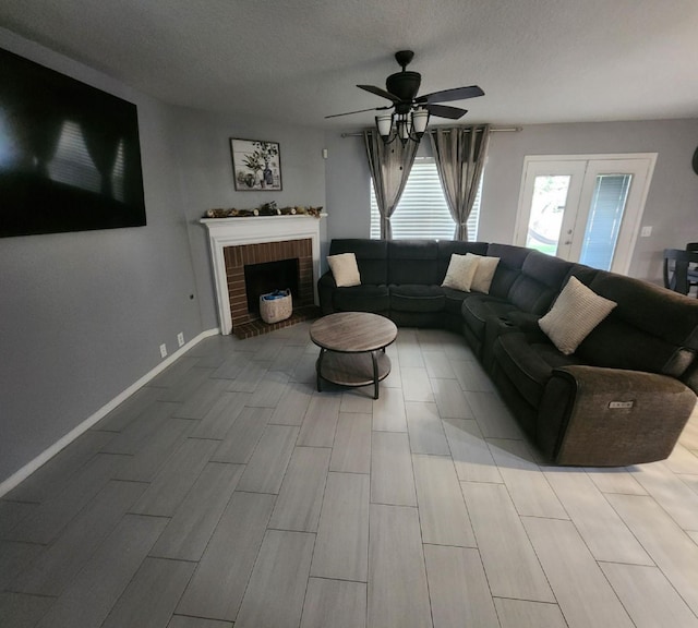 living room with a textured ceiling, ceiling fan, a fireplace, and french doors