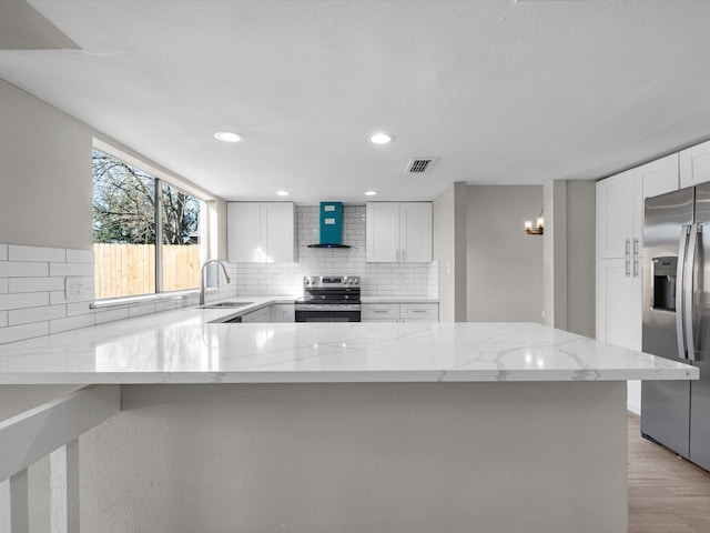 kitchen featuring white cabinets, appliances with stainless steel finishes, light stone counters, and wall chimney range hood