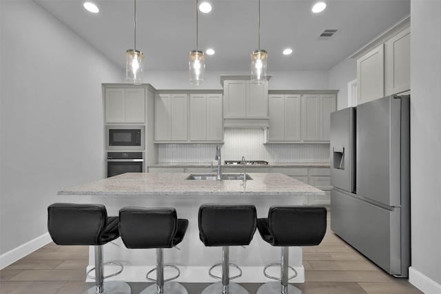 kitchen featuring backsplash, a center island with sink, sink, appliances with stainless steel finishes, and light stone counters