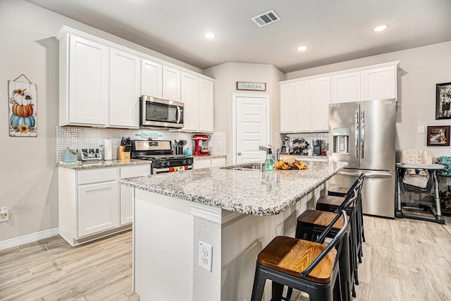 kitchen with appliances with stainless steel finishes, a kitchen island with sink, sink, and white cabinets