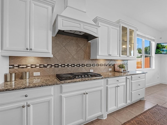 kitchen with wall chimney range hood, decorative backsplash, stainless steel gas cooktop, white cabinets, and dark stone countertops