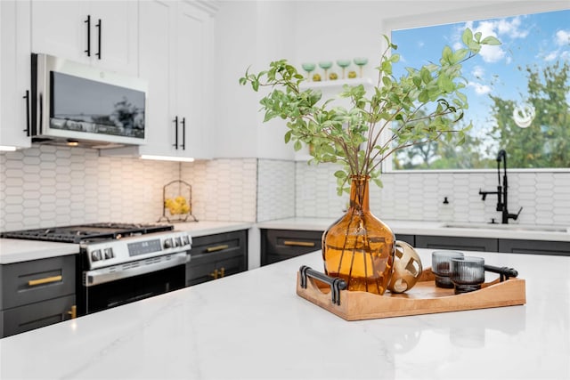 kitchen featuring light stone counters, stainless steel appliances, a sink, white cabinets, and tasteful backsplash