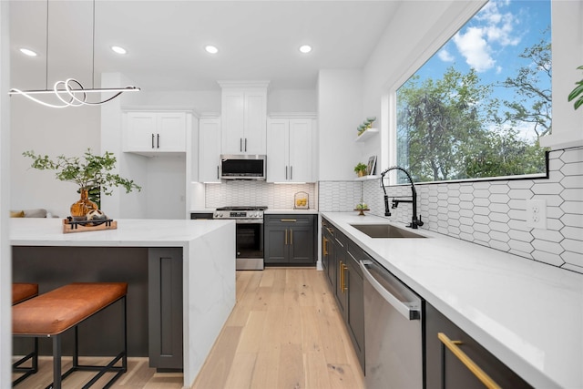 kitchen with a sink, white cabinetry, appliances with stainless steel finishes, light stone countertops, and open shelves