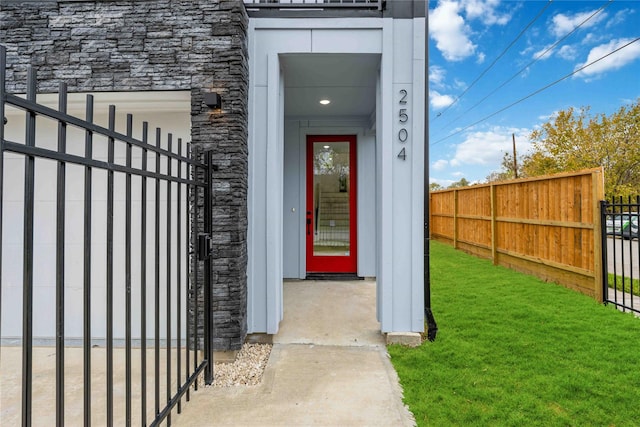 entrance to property with a yard, stone siding, and fence