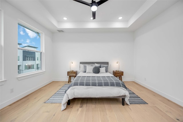 bedroom with a tray ceiling, visible vents, light wood-style flooring, and baseboards