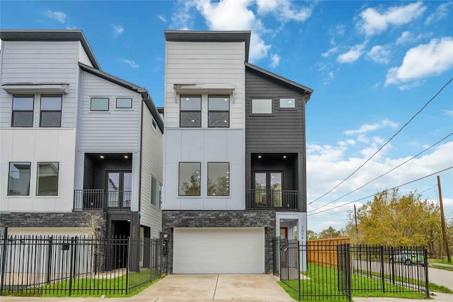 contemporary house featuring an attached garage, concrete driveway, stone siding, and fence