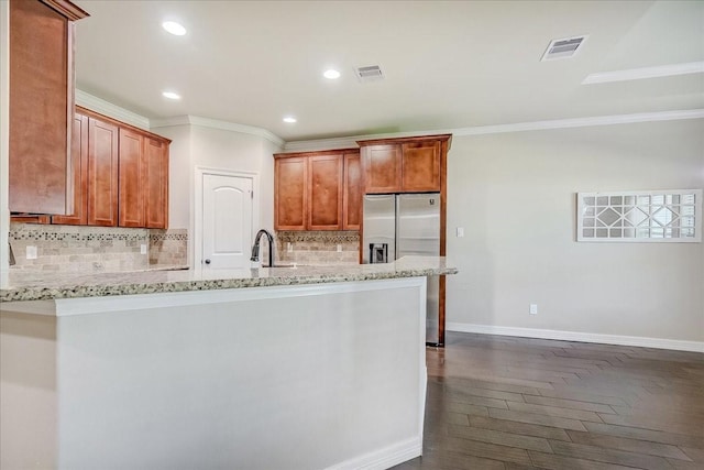 kitchen featuring stainless steel fridge, backsplash, light stone counters, ornamental molding, and dark hardwood / wood-style floors