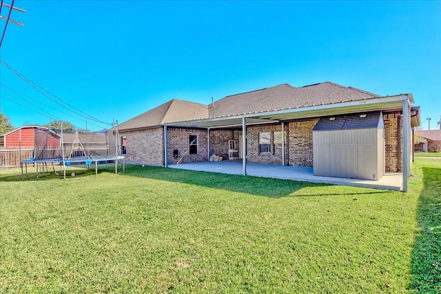 rear view of property with a lawn, a patio, and a trampoline