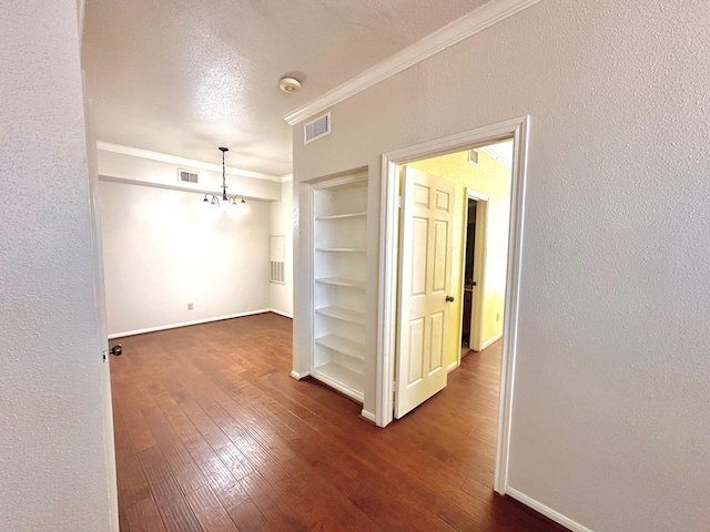 empty room featuring dark hardwood / wood-style flooring, built in features, a notable chandelier, a textured ceiling, and ornamental molding