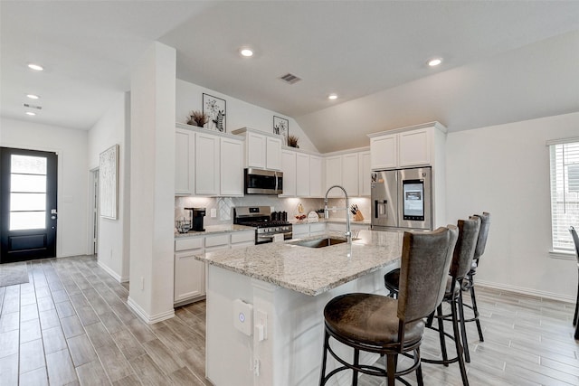 kitchen with stainless steel appliances, vaulted ceiling, sink, a center island with sink, and white cabinetry