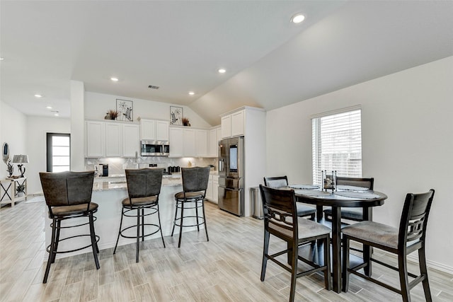 kitchen with white cabinetry, light stone countertops, stainless steel appliances, a kitchen breakfast bar, and lofted ceiling