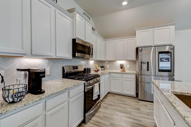 kitchen with decorative backsplash, light stone counters, white cabinetry, and appliances with stainless steel finishes