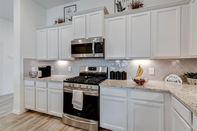 kitchen featuring decorative backsplash, light stone countertops, light wood-type flooring, stainless steel appliances, and white cabinets